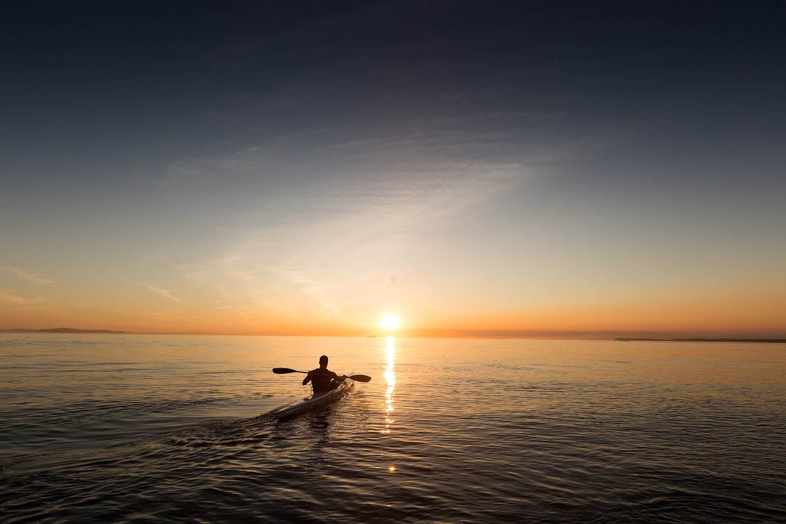 Kayaker silhouetted against a golden sunrise on flat calm water — the vibe of our Chuburná flamingo paddle