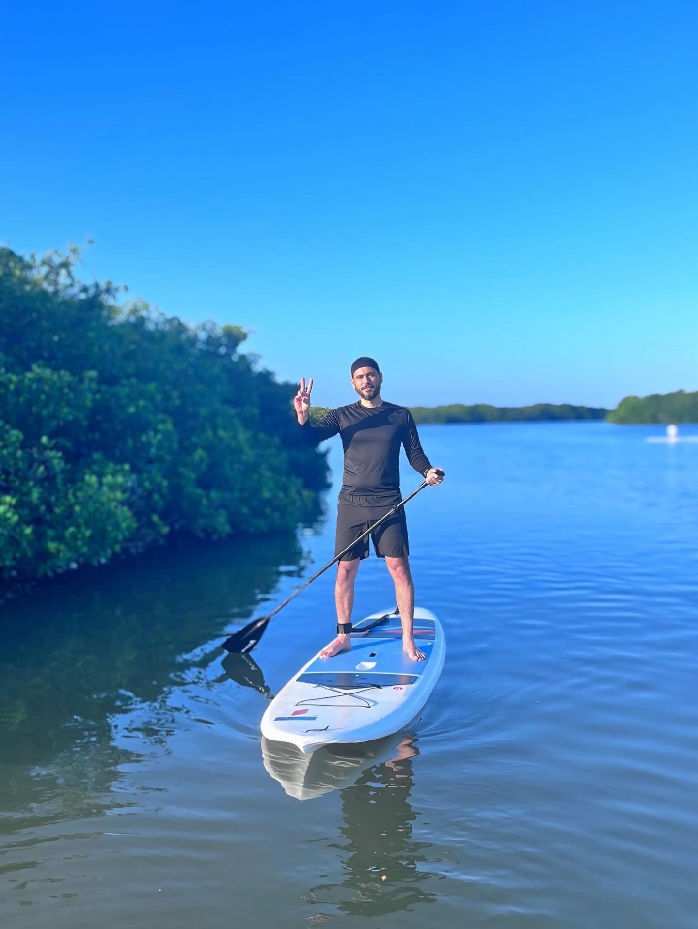 Paddleboarder de pie sobre la tabla junto al muro de manglar de Chelem bajo cielo azul despejado — condiciones de la salida de SUP de las 6:00 am en Progreso